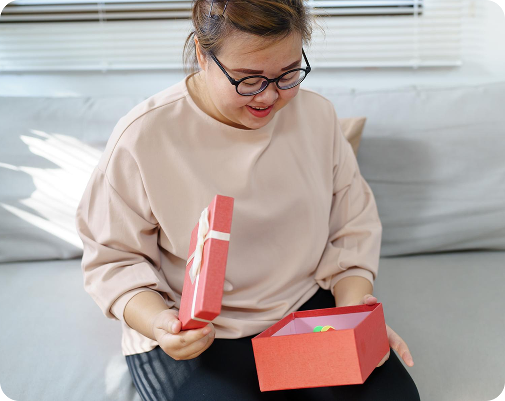 A woman smiling as she opens a wrapped gift box